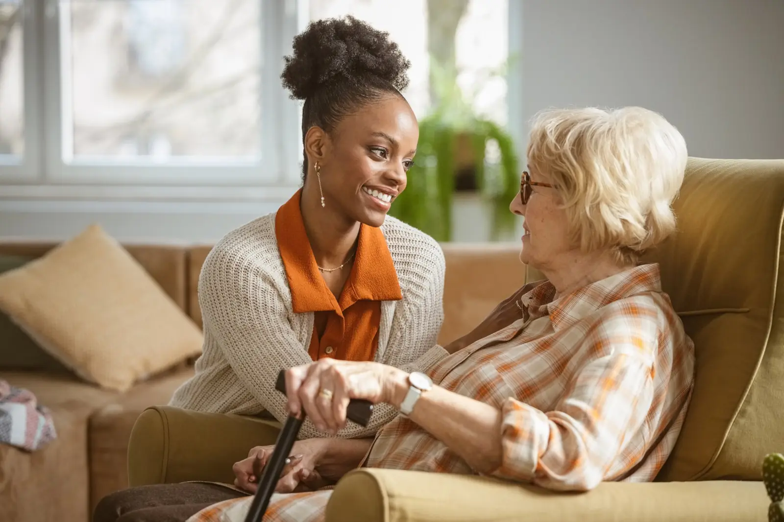 Caregiver kneeling beside a senior woman in her armchair