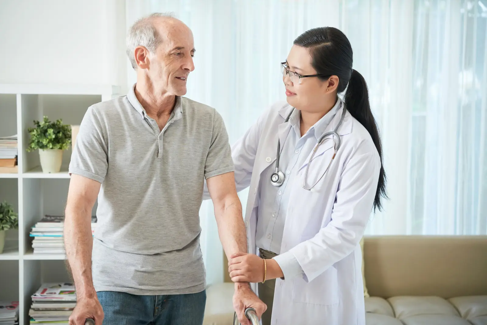 Clinician helping a senior man walk safely with a walker at home