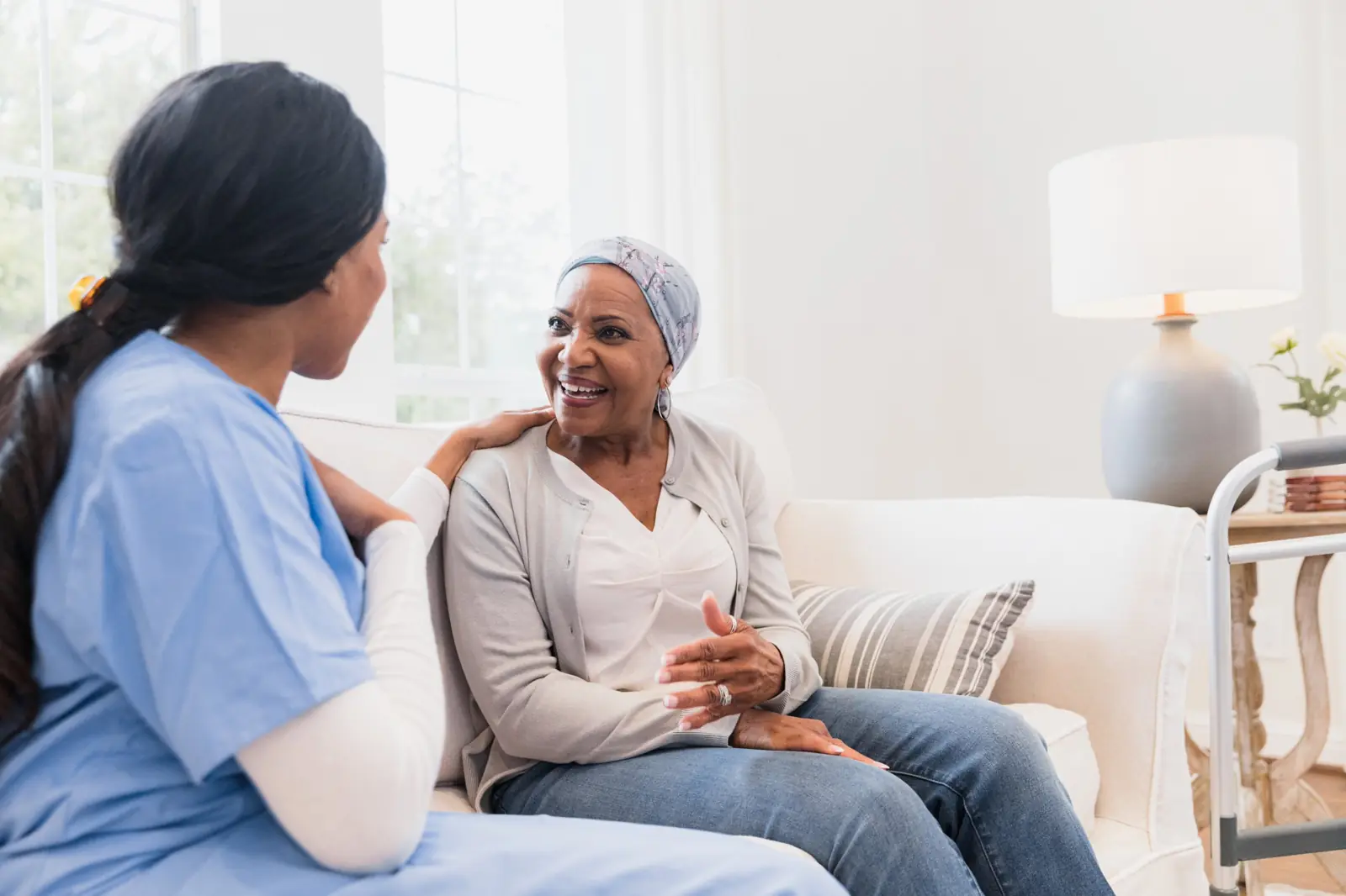 Home health nurse talking with a smiling patient on her sofa