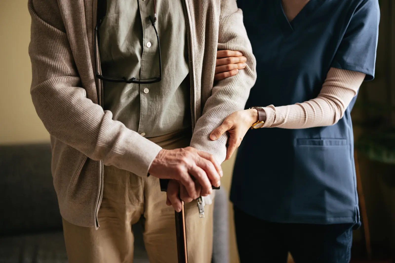 Home health nurse supporting a senior man with a cane after a hospital stay